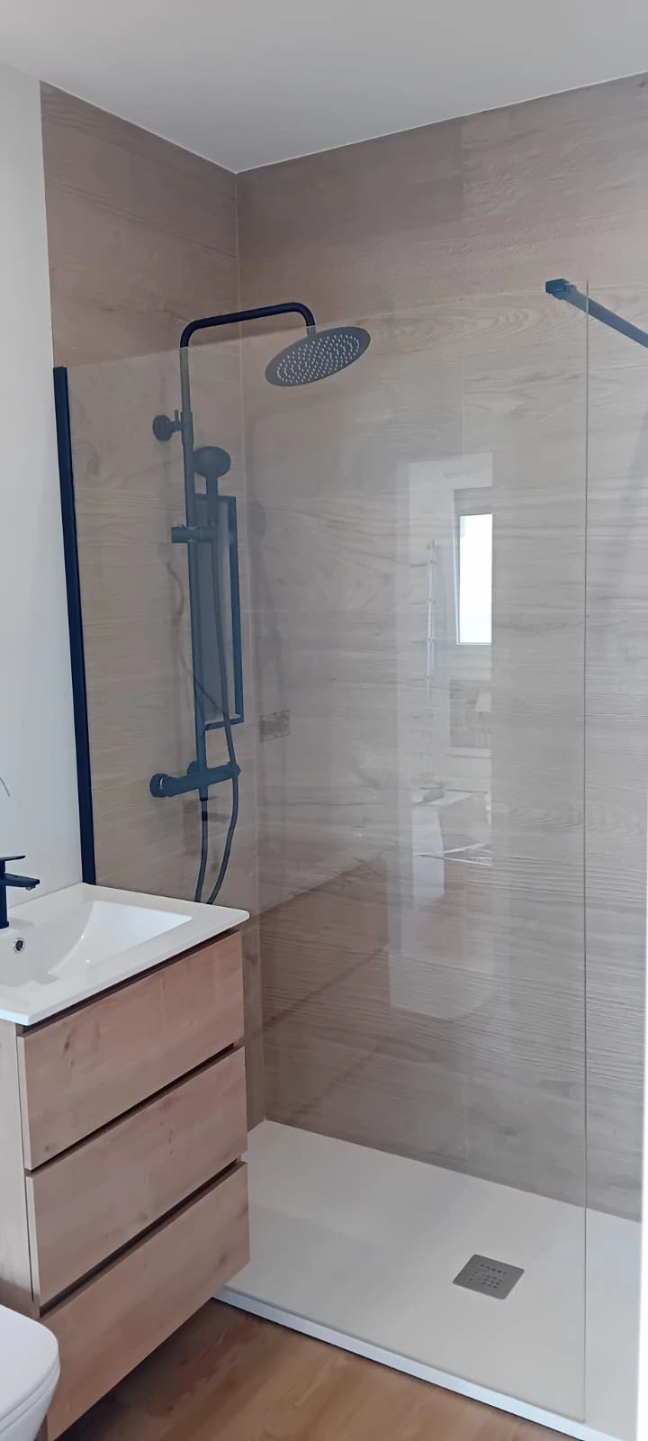 Reforma de baño con ducha de grifería negra y revestimiento cerámico imitación madera en Barakaldo