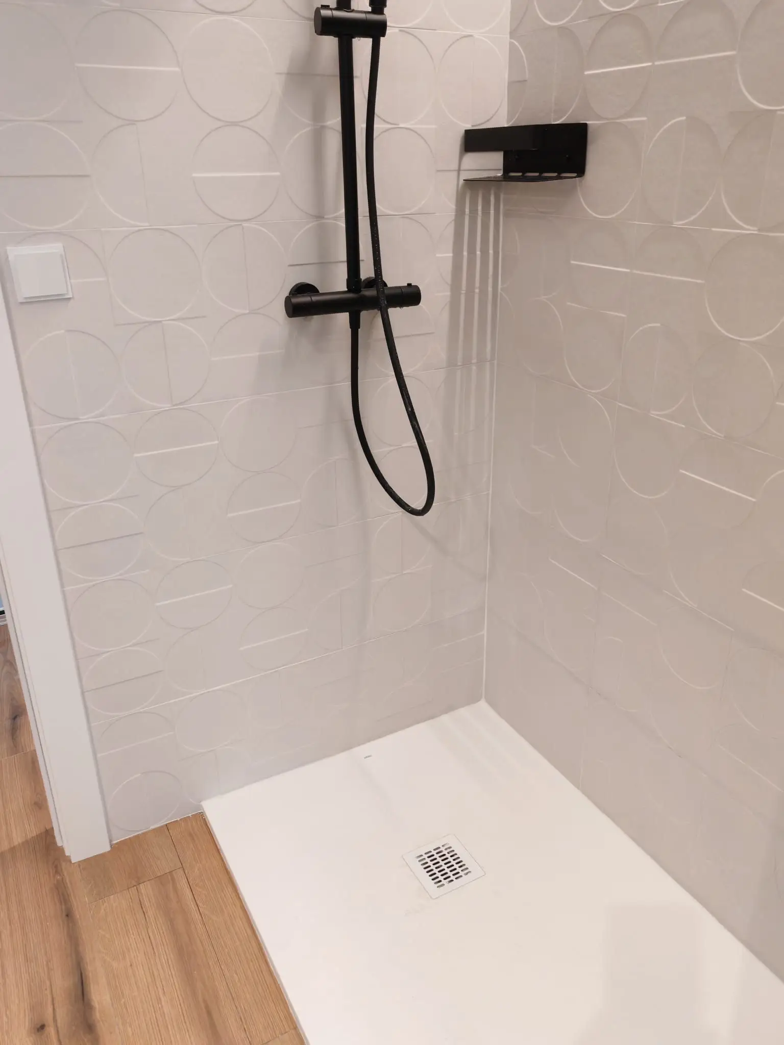 Reforma de baño con grifería negra mate y azulejos blancos con relieve geométrico en Barakaldo