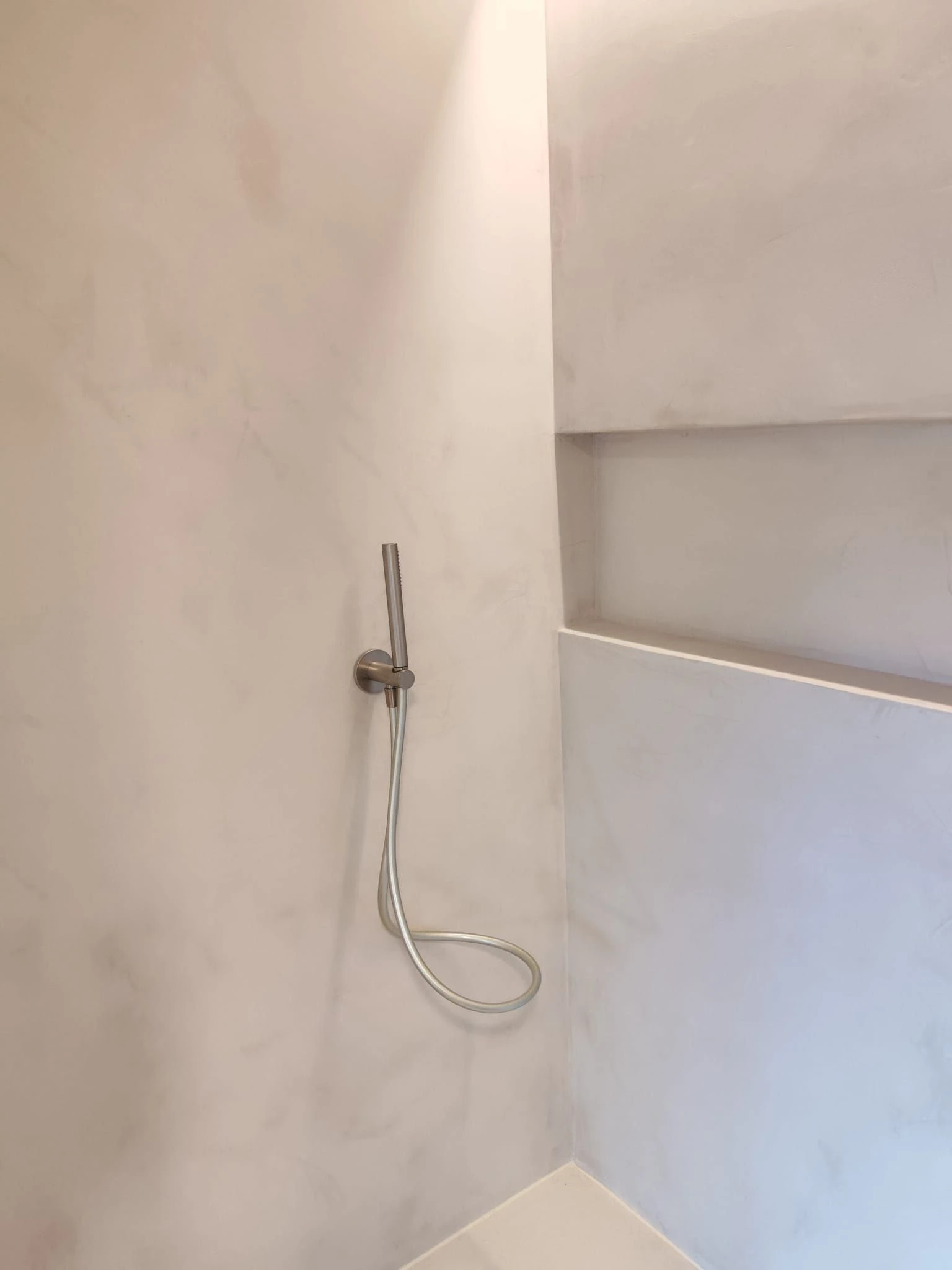 Reforma de baño con paredes de microcemento beige, hornacina integrada y grifería minimalista en Barakaldo