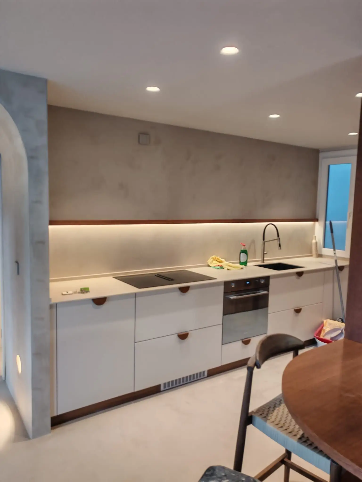 Reforma de cocina con pared de microcemento gris, muebles blancos y tira LED integrada en Barakaldo