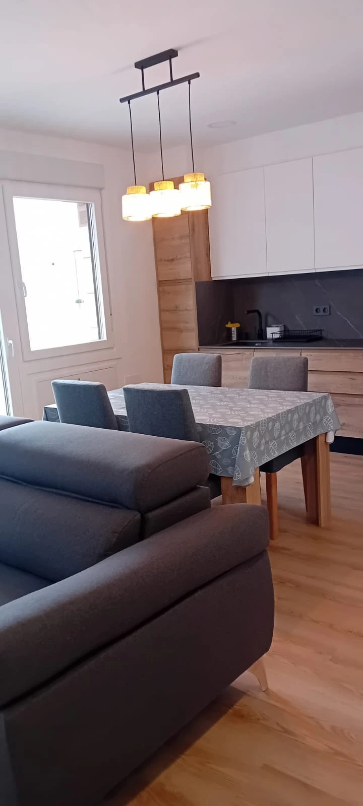 Reforma de vivienda con salón y cocina integrados mediante mobiliario de madera y tonos grises en Barakaldo